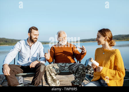 L'homme et la femme ayant la conversation chaleureuse avec des grand-père pendant le pique-nique près du lac, dans le matin Banque D'Images