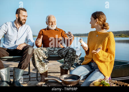L'homme et la femme ayant la conversation chaleureuse avec des grand-père pendant le pique-nique près du lac, dans le matin Banque D'Images