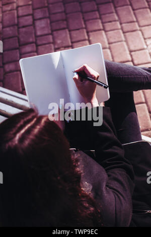 Fille brune travaillant sur son travail à faire à la dissertation ou mémoire de recherche et de mettre par écrit ses pensées sur un ordinateur portable qu'elle tient dans ses mains. Pav Banque D'Images