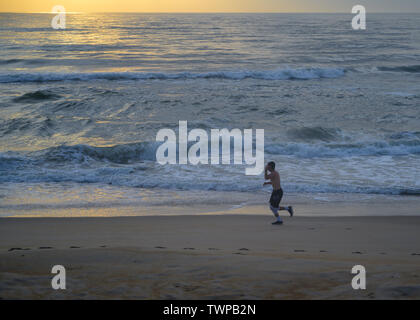 Canard, North Carolina, USA -- 10 juin 2019. Un homme en short est le jogging sur la plage de Caroline du Nord comme le soleil se lève sur l'Atlantique Ocea Banque D'Images