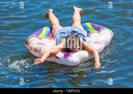 Iford, Dorset, UK. 22 juin 2019. Un temps magnifique, ensoleillé et chaud, toujours pour Dorset Canot Journée avec des centaines de jeux gonflables, des dériveurs, artisanat, conseils formant une flottille, de mettre les voiles de l'IFORD pont rivière Stour de Tuckton bridge. L'événement a commencé en 2014 comme un petit peu de plaisir, mais est maintenant devenu un événement annuel recueillant des fonds pour des organismes de bienfaisance et fonceur plus grand chaque année. Young woman relaxing on cupcake gonflable gonflable. Credit : Carolyn Jenkins/Alamy Live News Banque D'Images