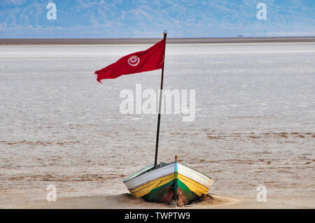 Un petit bateau abandonné avec drapeau rouge au milieu de Chott el Jerid salt lake en Tunisie Banque D'Images