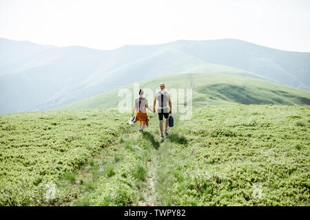 Couple en train de marcher avec des sacs sur le pré vert, voyager dans les montagnes en été, large vue paysage Banque D'Images