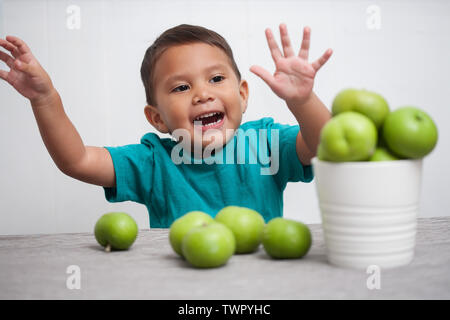 Un jeune garçon exprimant sa joie pour les fruits, les bras en l'air et jouer avec un seau de pommes vertes. Banque D'Images