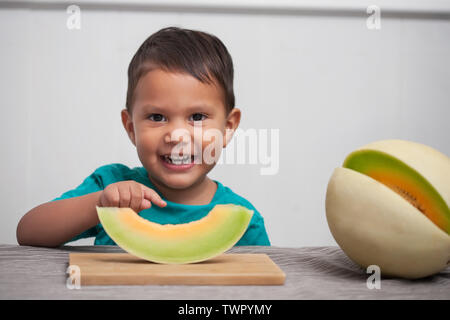 Un jeune enfant avec sourire mignon points à sa tranche d'un melon de miel il est sur le point de manger dans le cadre d'une collation santé. Banque D'Images