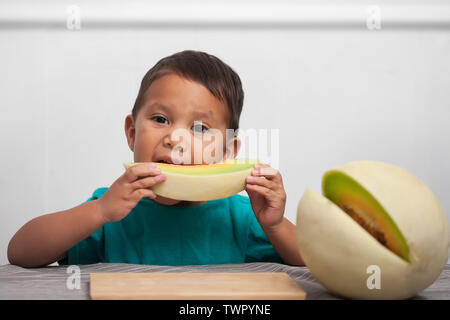 Un enfant de manger un morceau de fruit frais honeymelon sur son propre et bénéficiant d'une solution de rechange saine aux aliments transformés. Banque D'Images