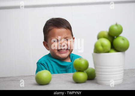 Jeune garçon souriant gaiement et assis en face d'un tas de pommes vertes. Banque D'Images