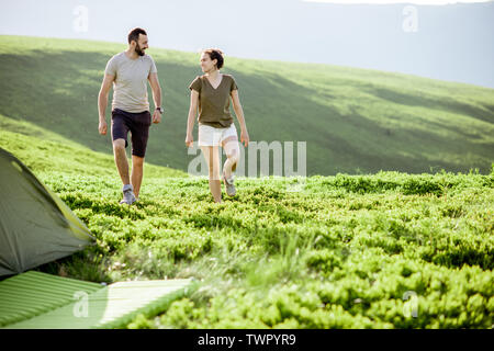 Jeune couple en train de marcher sur le pré vert à proximité du camping tout en voyageant dans les montagnes Banque D'Images