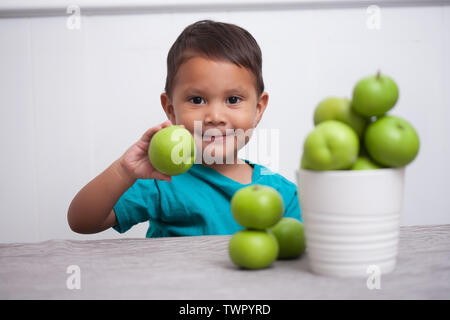 Un enfant heureux d'être titulaires d'une pomme verte de sa pile de pommes cueillies à la main. Banque D'Images