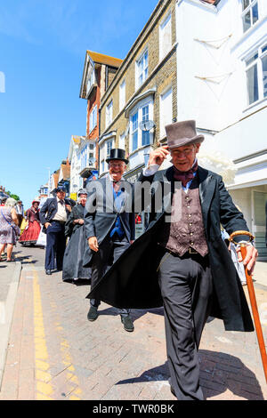 Broadstairs Dickens Festival. La parade principale le long de la rue principale, haute, avec des gens habillés en costume victorien, l'homme basculant la hat au spectateur. Banque D'Images