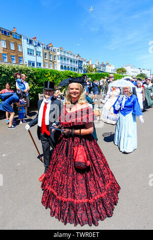 Festival annuel de Broadstairs Dickens. La parade principale sur la promenade du front de mer, avec des gens habillés en costume victorien comme caractères de Dickens. Femme mature en robe rouge foncé smiling at viewer comme elle marche vers. Banque D'Images