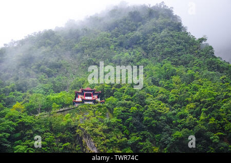 Magnifique temple chinois sur un rocher escarpé entouré de forêt tropicale. Par temps brumeux, le brouillard. Paysage de Taiwan, voyage en Chine. Caractère chinois. Beau culte, concept religieux. Banque D'Images