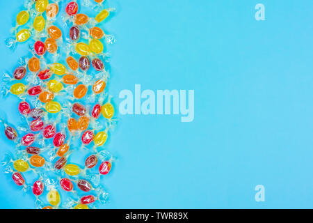 Bonbons multicolores lumineux dans des emballages transparents, des bonbons de mica sur fond bleu, des bonbons colorés dispersés, vue supérieure avec copie espace. Mise à plat Banque D'Images