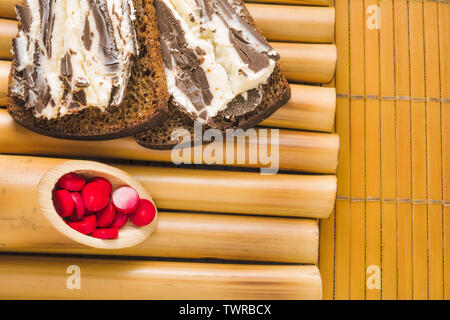 Sandwich avec pain de blé noir grossier et sweet curd et chocolat noir sur un stand de bambou et de bambou serviette avec perles de corail rouge. Il simple délicieux Banque D'Images