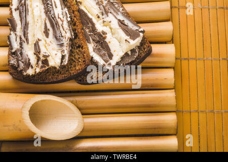 Sandwich avec pain de blé noir grossier et sweet curd et chocolat noir sur un stand de bambou et de bambou serviette. Délicieux petit déjeuner santé simple en e Banque D'Images