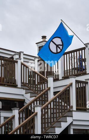 Drapeau bleu vif avec un signe de paix en noir et blanc sur le volant d'un post sur un escalier peint en blanc et bois Banque D'Images