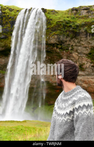 Pull homme islandais par cascade sur l'Islande outdoor en souriant. Portrait de la bonne recherche modèle masculin en nature paysage avec cascade de Seljalandsfoss attraction touristique sur Ring Road. Banque D'Images