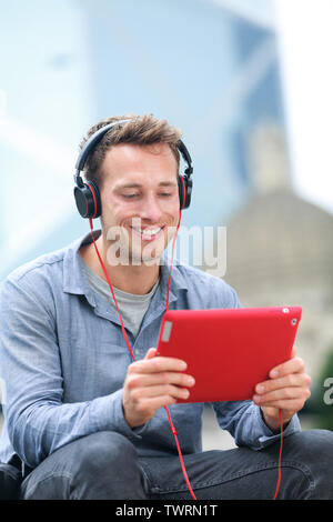 Conversation de chat vidéo. Man talking on tablet pc assis dehors à l'aide de l'app sur 4g sans fil portant des écouteurs de l'appareil. Casual young urban professional homme dans la fin des années 20. Banque D'Images