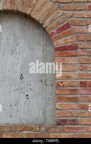 Vieille beige robuste mur parsemé de briques colorées de différentes teintes de rouge, montrant une fenêtre en brique barricadèrent Banque D'Images