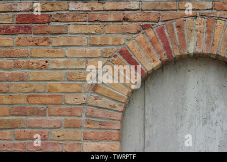 Vieille beige robuste mur parsemé de briques colorées de différentes teintes de rouge, montrant une fenêtre en brique barricadèrent Banque D'Images