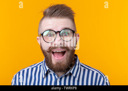 Jeune homme élégant hipster avec une moustache et barbe joyeusement ouvre la bouche sur un fond jaune. Concept de surprise et de célébration. Copyspace. Banque D'Images