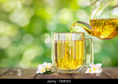 Thé au jasmin à base de coulage de théière en verre en cup sur table en bois avec fond naturel vert floue Banque D'Images