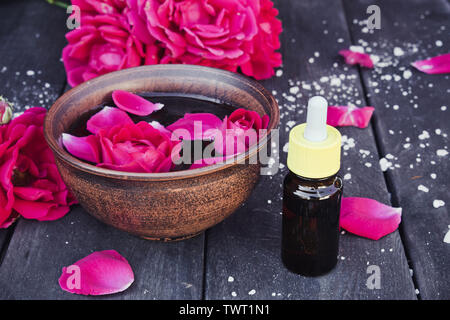 Près de l'huile essentielle de pétales de rose rouge bol avec sur un fond en bois sombre. L'aromathérapie. Banque D'Images