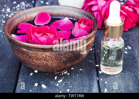 Près de l'huile essentielle de pétales de rose rouge bol avec sur un fond en bois sombre. L'aromathérapie. Banque D'Images