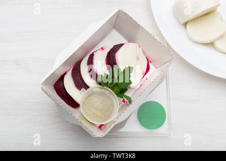 Vue de dessus de betteraves bouilli avec des tranches de fromage blanc se trouvent dans une boîte à lunch blanc avec sauce à la crème aigre et le persil sur un tableau blanc à côté de fromage de chèvre Banque D'Images