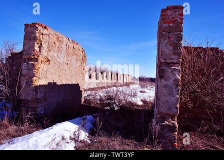 Coquina Crimée des blocs de roche ferme en ruine murs, résisté à sec pelouse couverte de neige, le sureau arbustes sans feuilles, bleu ciel clair backgroun Banque D'Images