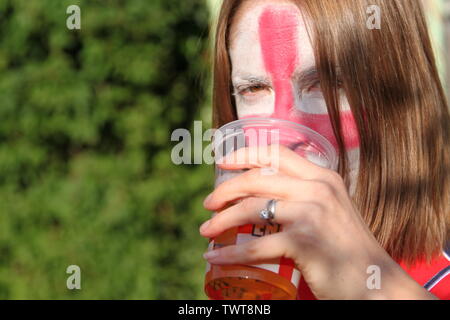 Angleterre, Royaume-Uni - gros plan d'une femme fan de football buvant avec un drapeau d'Angleterre de Saint-George peint sur le visage dans le jardin, un jour ensoleillé avec espace de copie Banque D'Images
