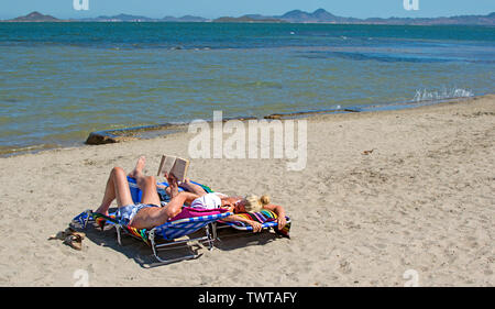 Murcia, Espagne - 22 juin 2019 : sur la plage tropicale de sable au cours de journée ensoleillée la lecture d'un livre et de dormir à des chaises de plage. Banque D'Images