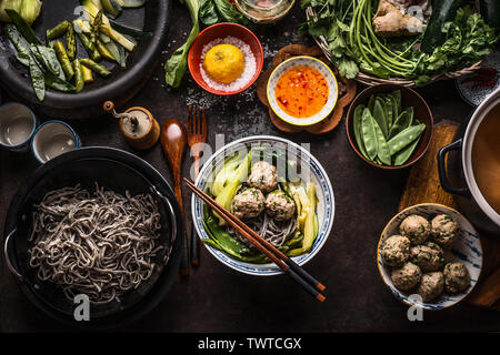 Bol à soupe de nouilles asiatique boulettes et baguettes sur la table de cuisine rustique foncé avec des légumes verts ingrédients. Pour la voir. La cuisine asiatique. Asian foo Banque D'Images