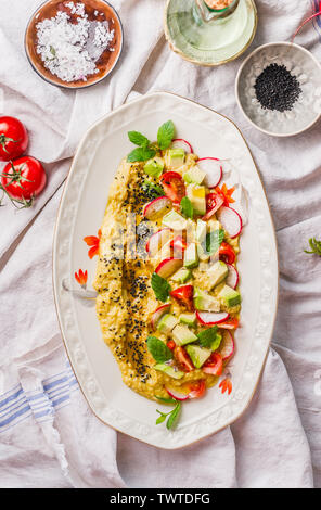 L'hummus maison surmontée de la plaque avec de l'huile d'olive, d'avocat, des légumes frais et des herbes sur une table de cuisine, vue d'en haut. La nourriture végane concept. Alimentation saine. Medite Banque D'Images