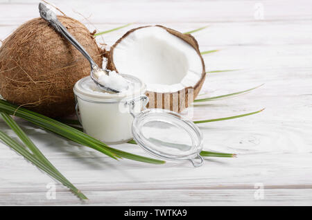 L'huile de noix de coco dans un bocal en verre hermétique et cuillère en bois blanc sur les plaques tableau Banque D'Images