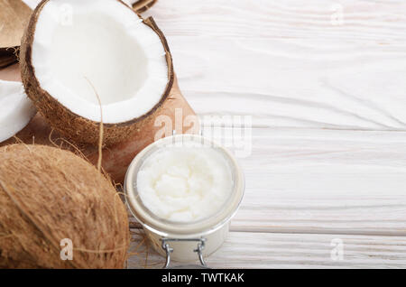 L'huile de noix de coco dans un bocal en verre hermétique et les plaques sur la table en bois blanc libre Banque D'Images