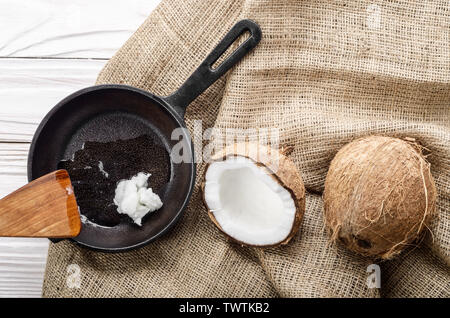 Coquille de noix de coco, avec de la viande, poêle en fonte et la spatule sur le chanvre sacs sur une table de cuisine en bois blanc Banque D'Images