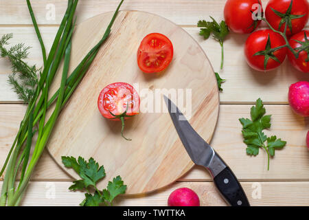 Concept de la nourriture végétarienne La cuisine. Conseil de cuisine ronde avec des tranches de tomate et de couteau sur elle. Les tomates cerises, oignon, radis, persil et aneth leafs l Banque D'Images