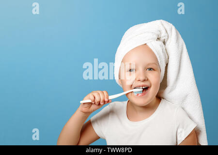 Closeup portrait d'une petite fille sur un fond bleu. Un enfant avec une serviette blanche sur sa tête se brosser les dents. Le concept de l'hygiène quotidienne. Banque D'Images