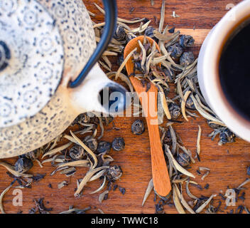 Un gros plan d'une théière et tasse de thé rouge, le thé vert et le thé blanc feuilles sur une table en bois Banque D'Images