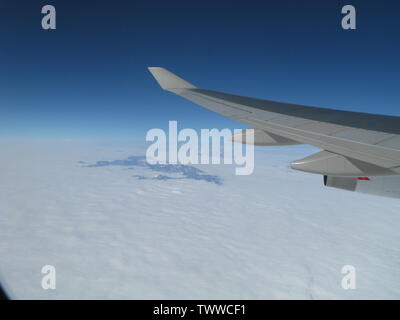 Vue depuis le côté gauche d'un Boeing 757 à l'aile. Sur les nuages et les montagnes au loin. Ciel bleu au-dessus. Banque D'Images