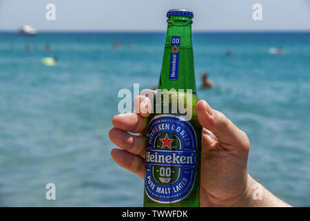 Main tenant zéro alcool Heineken bière bouteille par la mer. La bière sans alcool sur une bouteille en verre de 33cl avec plage floue sur la mer arrière-plan. Banque D'Images