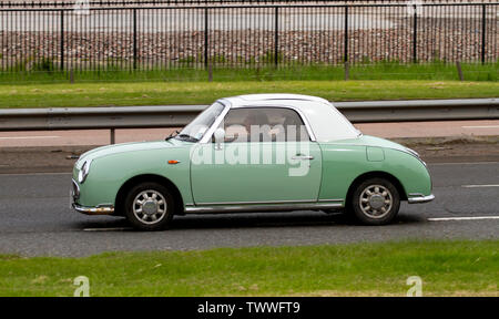 A senior woman driving un style rétro des années 60, le japonais Nissan Figaro voiture le long de la Kingsway à deux voies dans Dundee, Royaume-Uni Banque D'Images