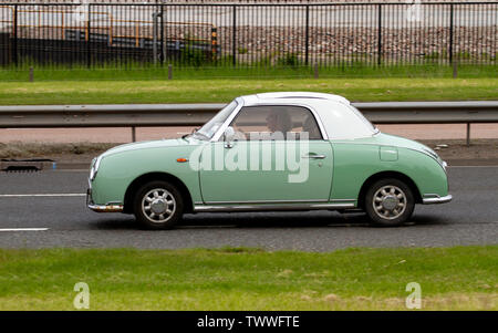 A senior woman driving un style rétro des années 60, le japonais Nissan Figaro voiture le long de la Kingsway à deux voies dans Dundee, Royaume-Uni Banque D'Images