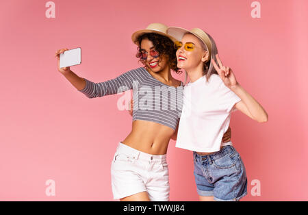 Deux jeunes femmes prenant diverses gaies sur smartphone selfies Banque D'Images