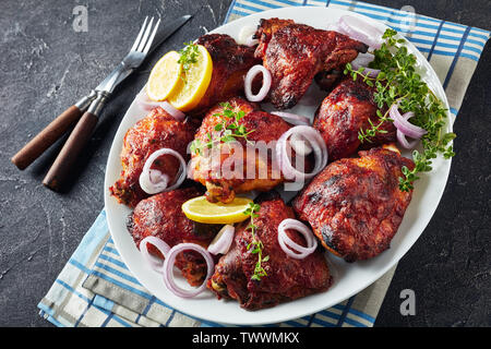 Vue de dessus de petites cuisses de poulet frit servi avec du thym, l'ail et l'échalote, les rondelles de citron sur une plaque blanche sur une table en béton, voir f Banque D'Images