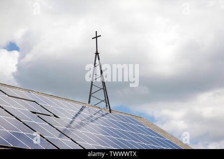 Une croix de métal sur le dessus d'un toit, avec des panneaux solaires rayons capture parmi les nuages Banque D'Images