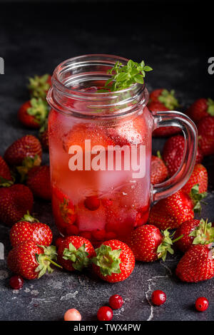 Boisson froide avec des fraises et de la glace en pot avec un décor de basilic, avec près de baies sur fond noir Banque D'Images