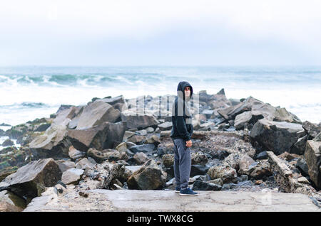Homme debout sur le rocher au milieu de l'océan. Article touristique au bord de la mer à la recherche de l'appareil photo Banque D'Images