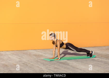 Young woman practicing yoga, faisant pousser ups ups ou appuyer sur l'exercice, phalankasana, planche, de travail, le port des vêtements de sport, pantalon noir et t Banque D'Images